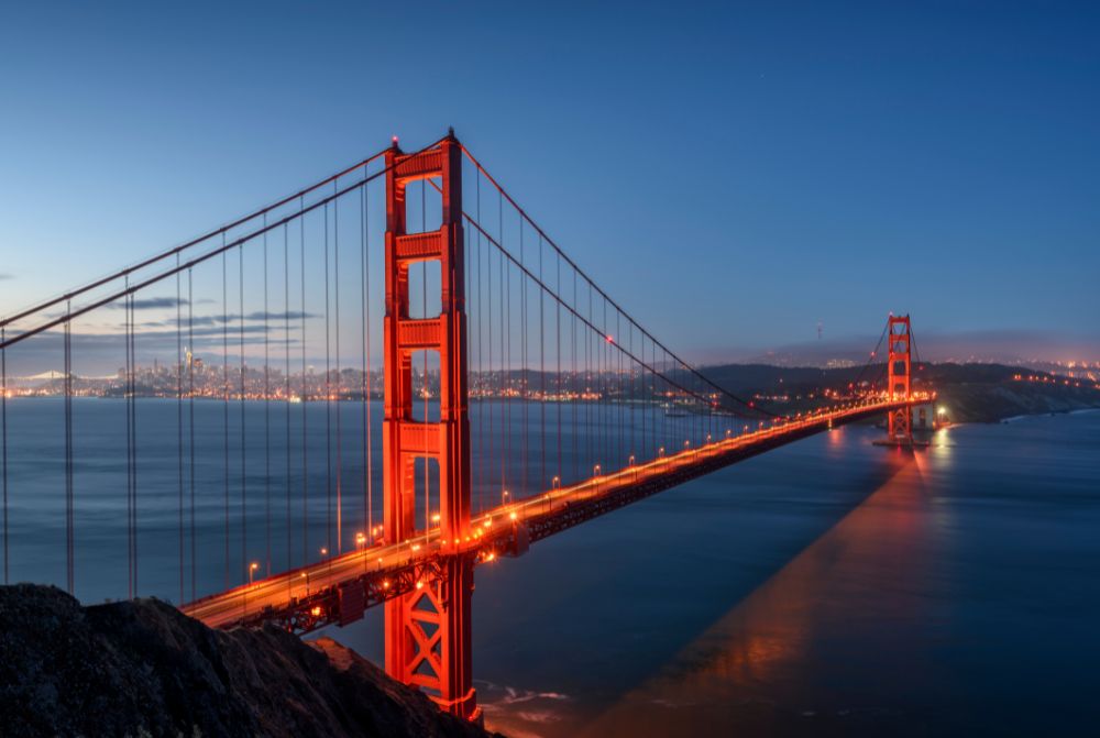 Golden Gate Bridge spanning over San Francisco Bay, with its iconic red-orange towers and suspension cables standing tall against a clear blue sky.